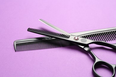Photo of Scissors and comb on violet background, closeup. Hairdresser's tools