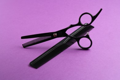 Photo of Scissors and comb on violet background, closeup. Hairdresser's tools