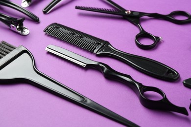 Photo of Different hairdresser's tools on violet background, closeup