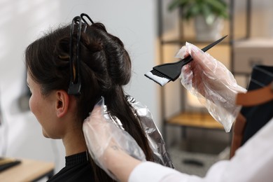 Photo of Hairdresser dyeing woman's hair in salon, closeup