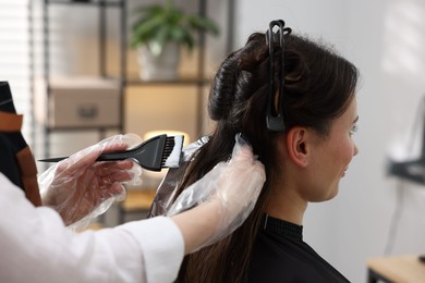 Photo of Hairdresser dyeing woman's hair in salon, closeup