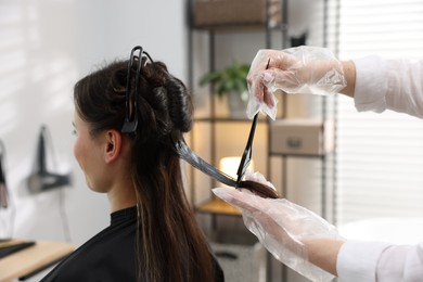 Photo of Hairdresser dyeing woman's hair in salon, closeup