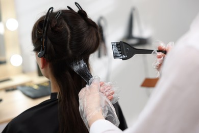 Photo of Hairdresser dyeing woman's hair in salon, closeup