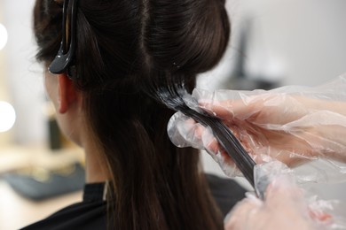 Photo of Hairdresser dyeing woman's hair in salon, closeup