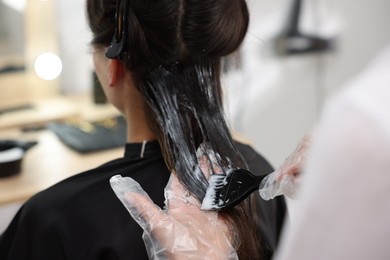 Photo of Hairdresser dyeing woman's hair in salon, closeup
