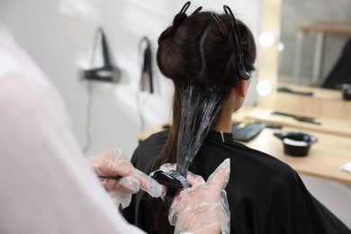 Photo of Hairdresser dyeing woman's hair in salon, closeup