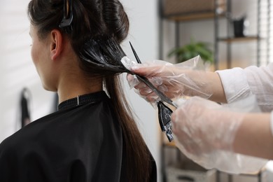 Photo of Hairdresser dyeing woman's hair in salon, closeup