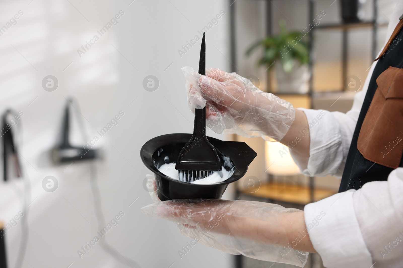 Stylist with bowl of hair dye and brush indoors, closeup Photo of Stylist with bowl of hair dye and brush indoors, closeup