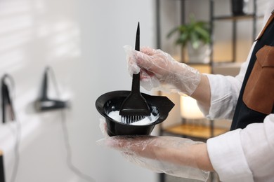 Photo of Stylist with bowl of hair dye and brush indoors, closeup