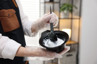 Photo of Stylist with bowl of hair dye and brush indoors, closeup