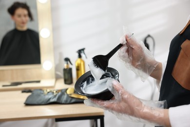 Photo of Stylist with bowl of hair dye and brush indoors, closeup