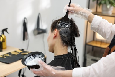 Photo of Hairdresser dyeing woman's hair in salon, closeup
