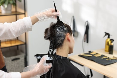 Photo of Hairdresser dyeing woman's hair in salon, closeup