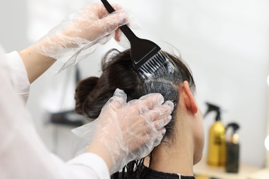 Photo of Hairdresser dyeing woman's hair in salon, closeup