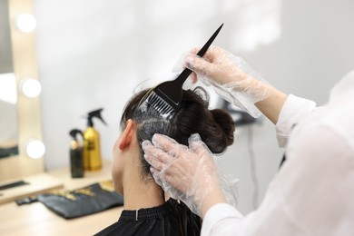 Photo of Hairdresser dyeing woman's hair in salon, closeup