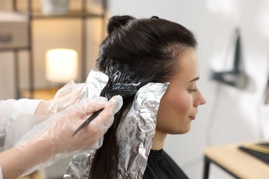 Photo of Hairdresser dyeing woman's hair in salon, closeup