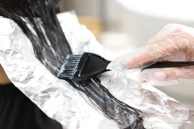 Photo of Hairdresser dyeing woman's hair in salon, closeup