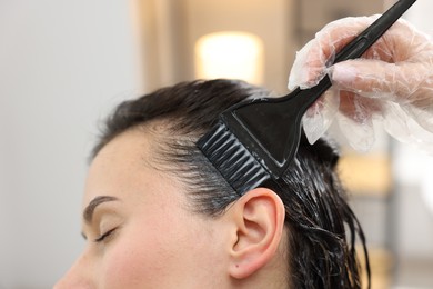 Photo of Hairdresser dyeing woman's hair in salon, closeup