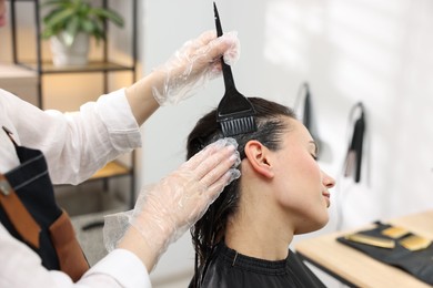 Photo of Hairdresser dyeing woman's hair in salon, closeup