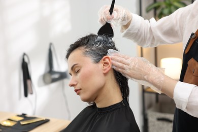 Photo of Hairdresser dyeing woman's hair in salon, closeup