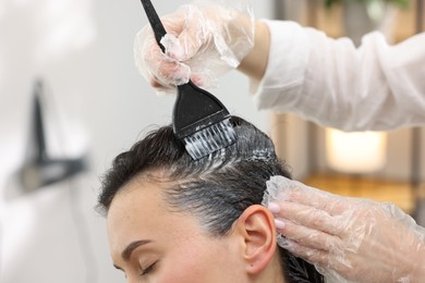 Photo of Hairdresser dyeing woman's hair in salon, closeup