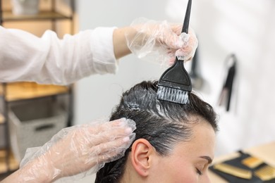 Photo of Hairdresser dyeing woman's hair in salon, closeup