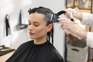 Photo of Hairdresser dyeing woman's hair in salon, closeup
