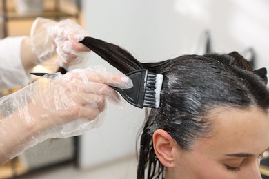 Photo of Hairdresser dyeing woman's hair in salon, closeup