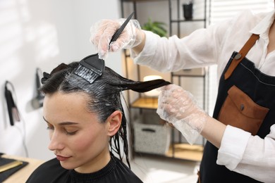 Photo of Hairdresser dyeing woman's hair in salon, closeup