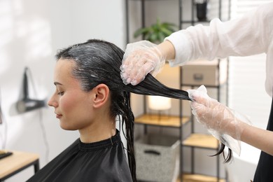 Photo of Hairdresser dyeing woman's hair in salon, closeup
