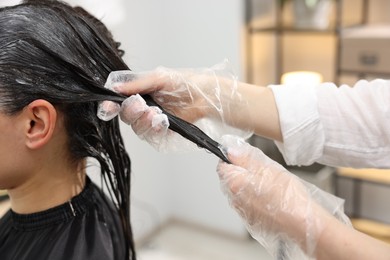 Photo of Hairdresser dyeing woman's hair in salon, closeup