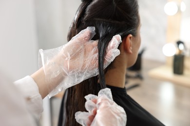 Photo of Hairdresser dyeing woman's hair in salon, closeup