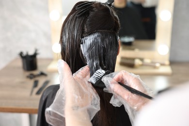 Photo of Hairdresser dyeing woman's hair in salon, closeup