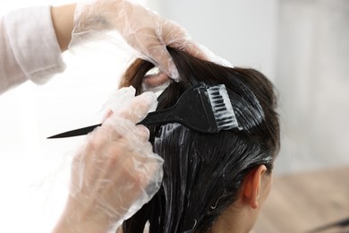 Photo of Hairdresser dyeing woman's hair in salon, closeup