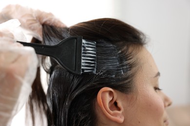 Photo of Hairdresser dyeing woman's hair in salon, closeup