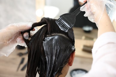 Photo of Hairdresser dyeing woman's hair in salon, closeup