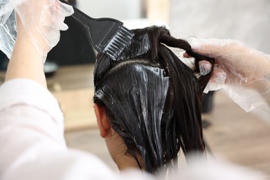 Photo of Hairdresser dyeing woman's hair in salon, closeup