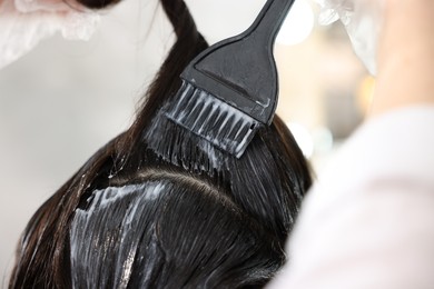 Photo of Hairdresser dyeing woman's hair in salon, closeup