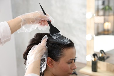 Photo of Hairdresser dyeing woman's hair in salon, closeup