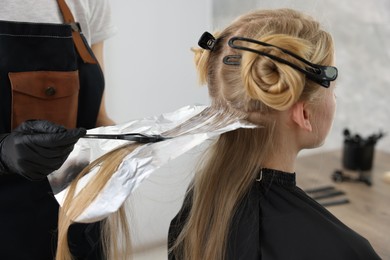 Photo of Hairdresser applying dye on woman's hair in salon, closeup