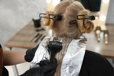 Photo of Hairdresser applying dye on woman's hair in salon, closeup