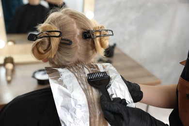 Photo of Hairdresser applying dye on woman's hair in salon, closeup