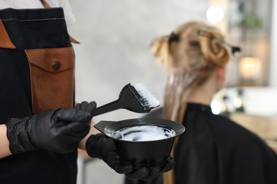 Photo of Hairdresser applying dye on woman's hair in salon, closeup