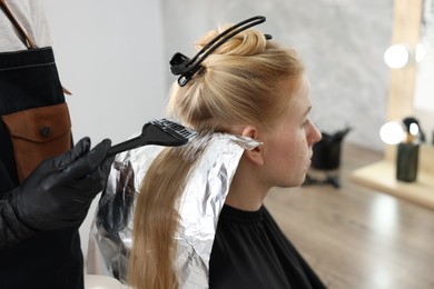Photo of Hairdresser applying dye on woman's hair in salon, closeup