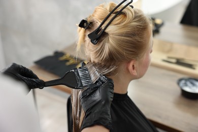 Photo of Hairdresser applying dye on woman's hair in salon, closeup