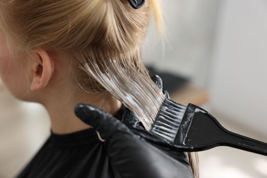 Photo of Hairdresser applying dye on woman's hair in salon, closeup