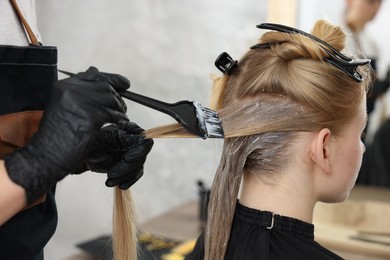 Photo of Hairdresser applying dye on woman's hair in salon, closeup