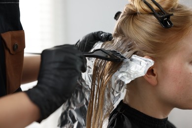 Photo of Hairdresser applying dye on woman's hair in salon, closeup