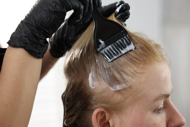 Photo of Hairdresser applying dye on woman's hair in salon, closeup