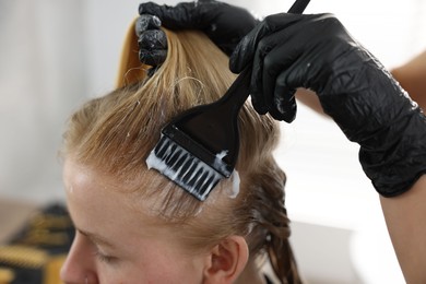 Photo of Hairdresser applying dye on woman's hair in salon, closeup